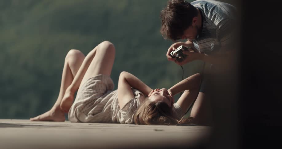 A man photographs his girlfriend as she lies on a dock in the sunshine