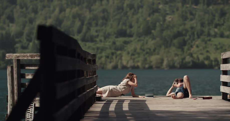 Young couple taking pictures over the wooden pier in the lake near the mountains
