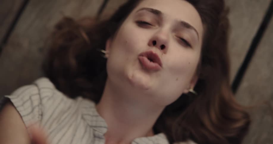 Happy woman resting over the planks of a wooden floor throws kisses at the camera