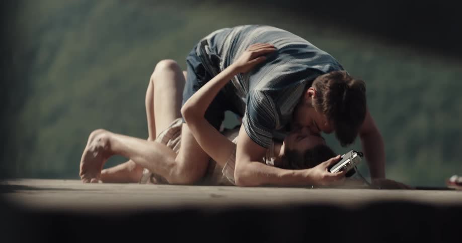 Young couple taking pictures and kissing while resting on a pier in the mountains