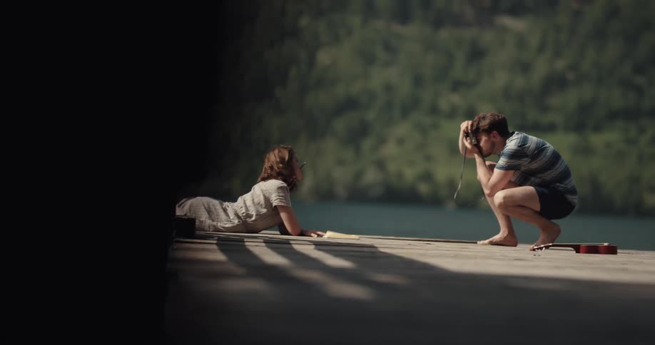 Young couple taking photographs on a wooden pier in the lake on the mountains