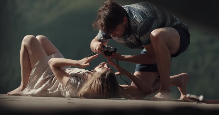A man with a camera taking a picture of a woman laying on a dock and kissing her