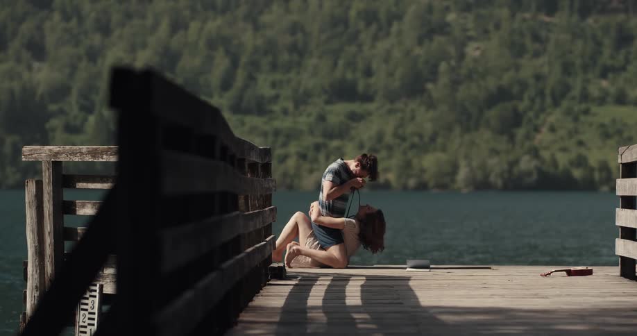 A man tries to take a photograph of his girlfriend as they play around while lying on a pier over a lake