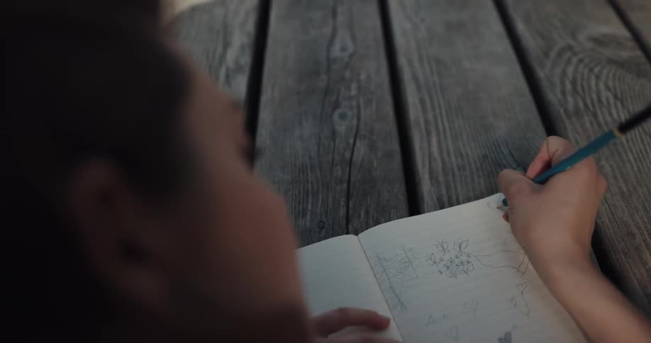 A young woman writing and doodling in a notebook while lying on her stomach