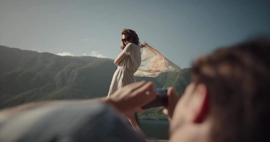 A man is photographing a woman as she dances by the lake