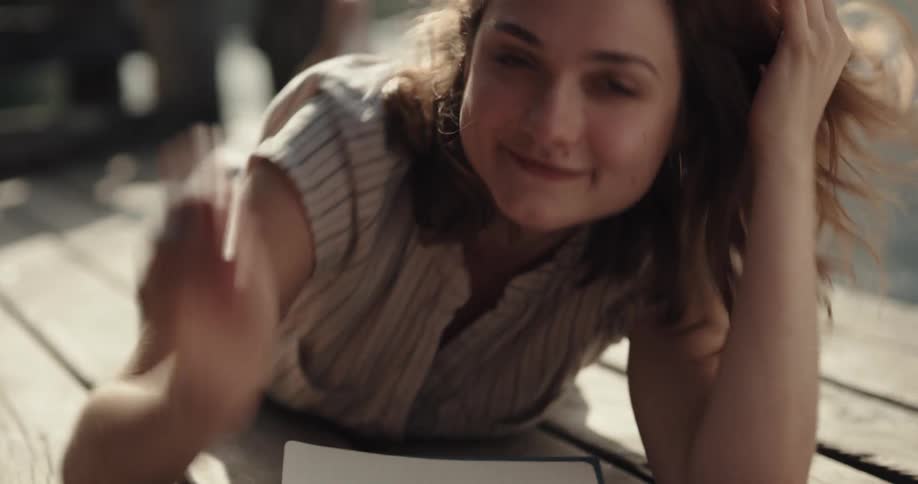 A woman is laying on a pier and posing with a pen and paper