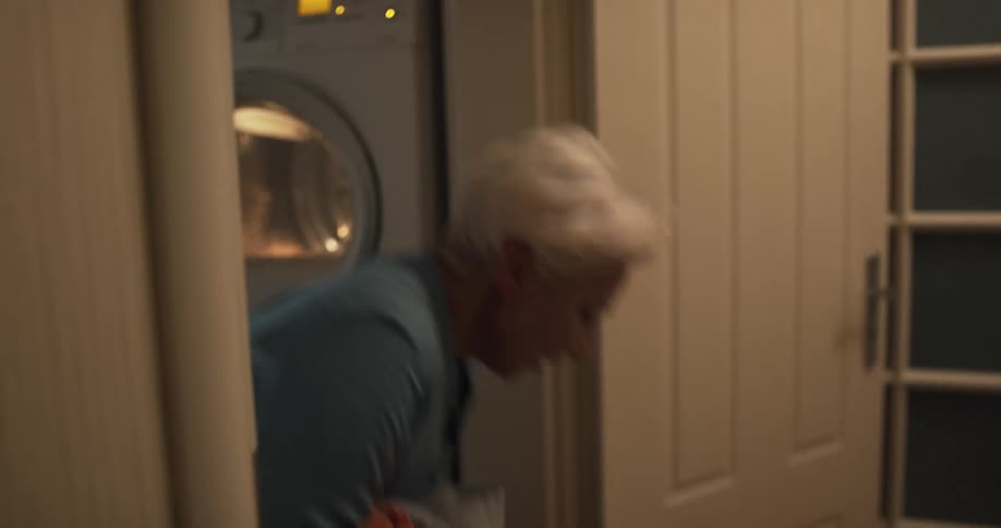 Woman loading laundry on a washing machine at home gets startled when someone throws dirty clothes at her