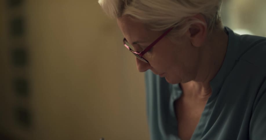 Elderly woman wearing glasses writes in a notebook with a pen