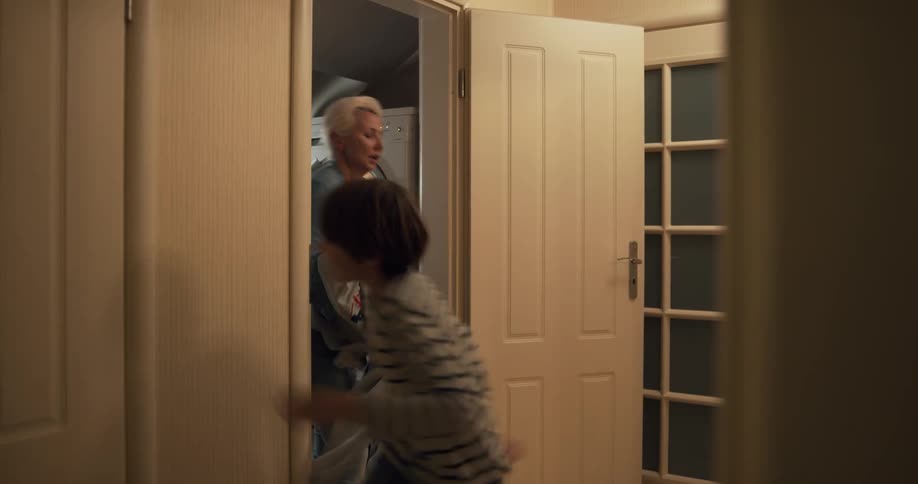 Boy runs in and throws clothes to woman doing laundry in laundry room