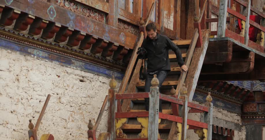 A man with a camera carefully walks down the steps of an old buddhist temple