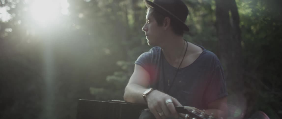 A man sits outside with a guitar on his lap