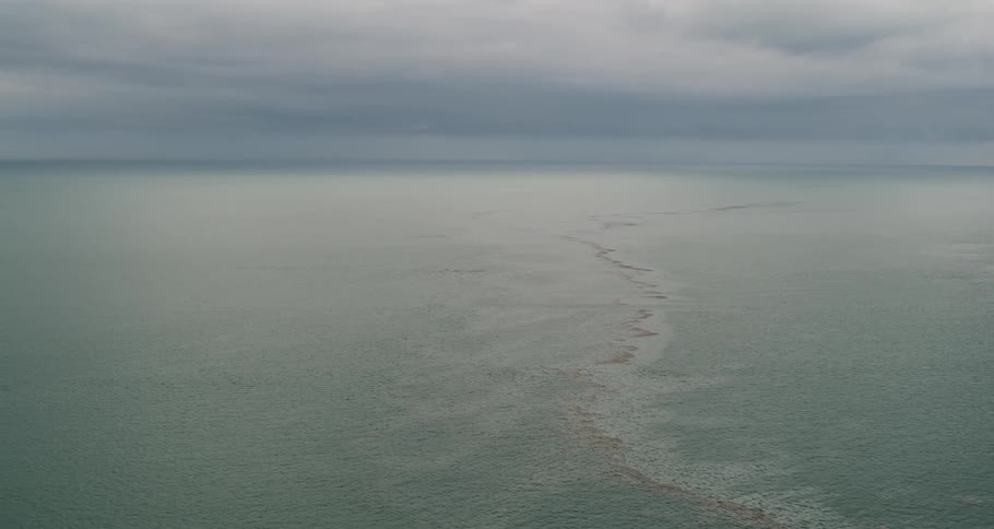 Waves moving across the water under a hazy cloudy sky