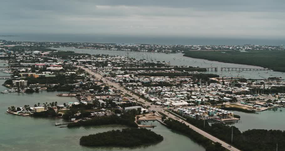 Traffic flows down road on strip of land in middle of water leading toward ocean on horizon