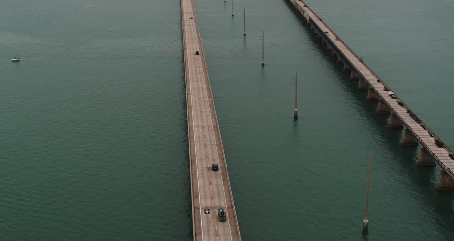 Vehicles travel across a long bridge over the ocean during the day