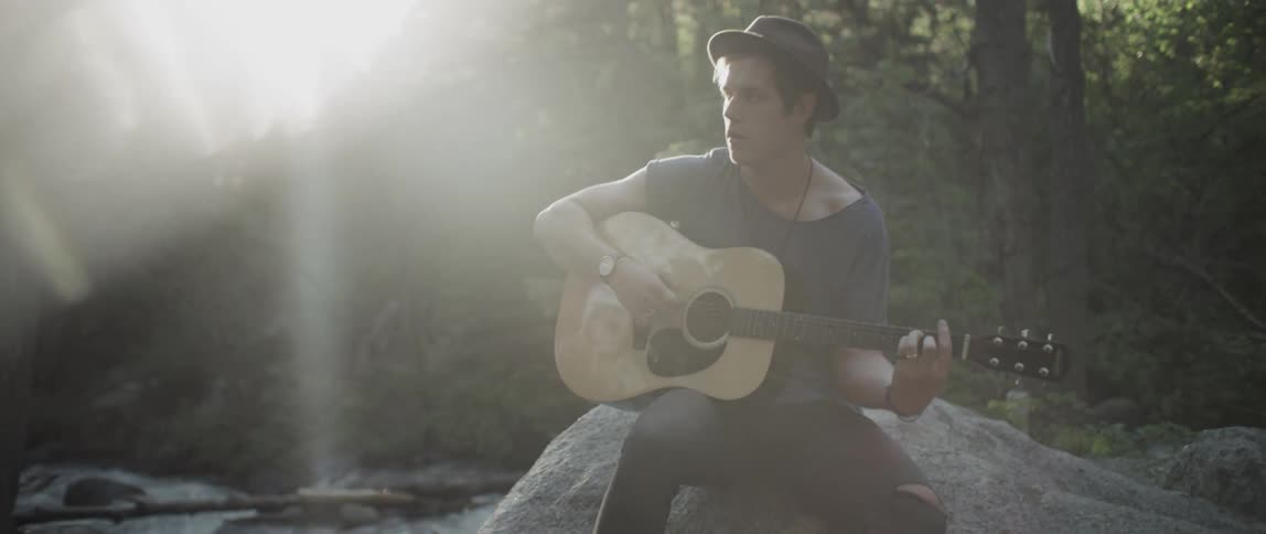 A man is sitting on a rock playing a guitar