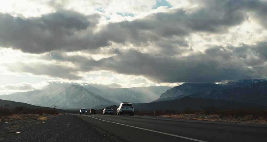 Traffic on a road with mountains in the distance under a cloud filled sky