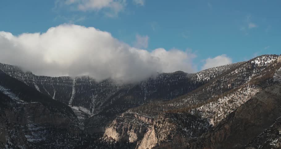 Light snow on a mountain forest under a cloud filled blue sky