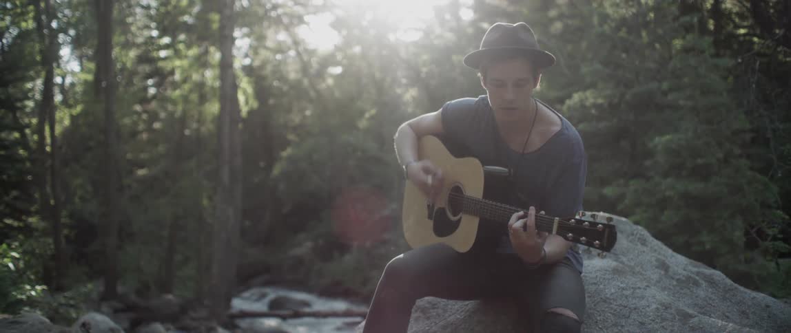 A man plays guitar on a rock in the forest