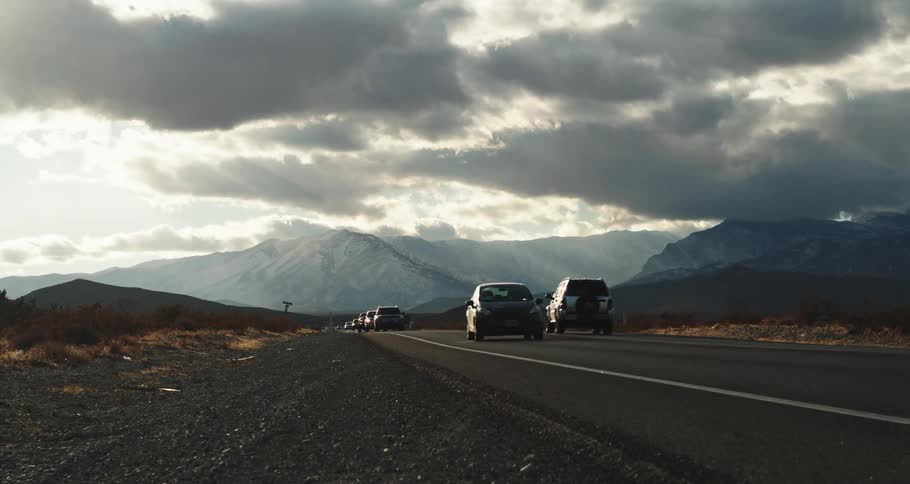 Traffic on a road with mountains in the distance under a cloud filled sky