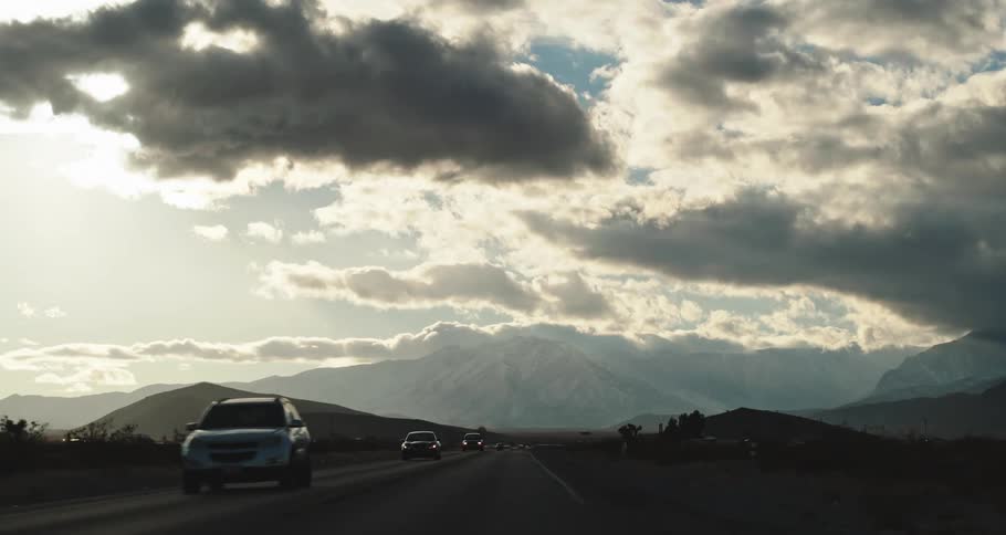 Traffic on a road with mountains in the distance under a cloud filled sky