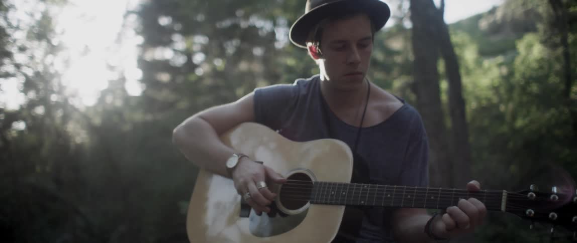 Man in a hat and t-shirt playing his guitar in the wilderness