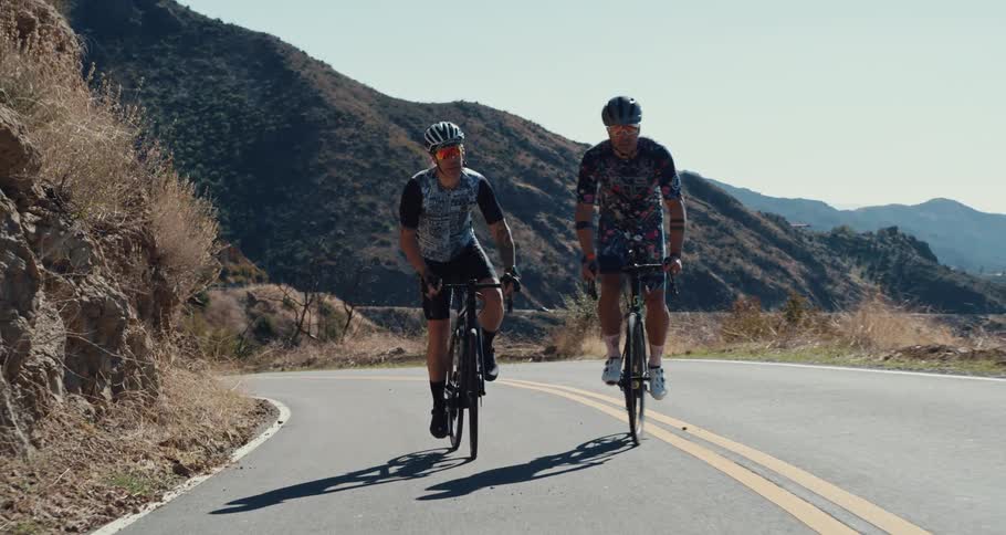 Two men are biking on a road next to mountains