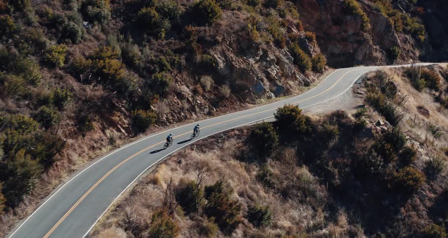 Two people cycle on a mountain road