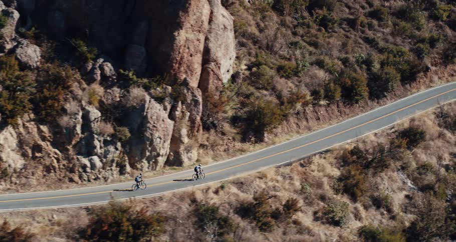 A pair of cyclist ride their bicycles along an arid mountain pass during the day