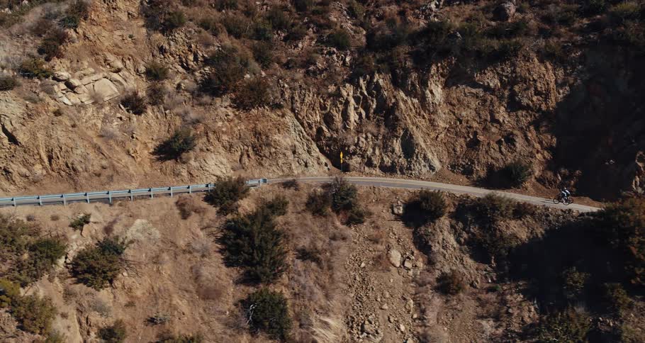 A pair of cycles ride their bicycles along a pass on an arid mountain during the day