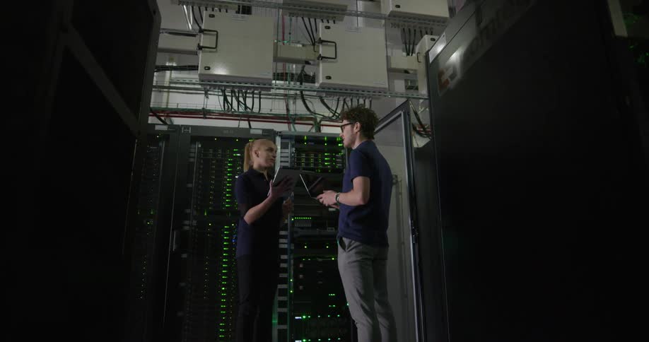 Two technicians speak with each other while standing within a data center filled with multiple data servers