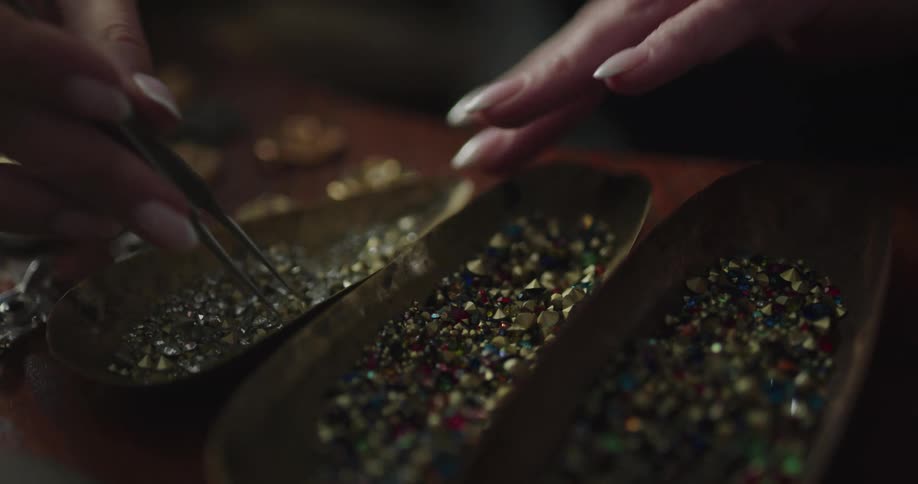 Woman with long fingernails looks through gems in three long bowls with tweezers