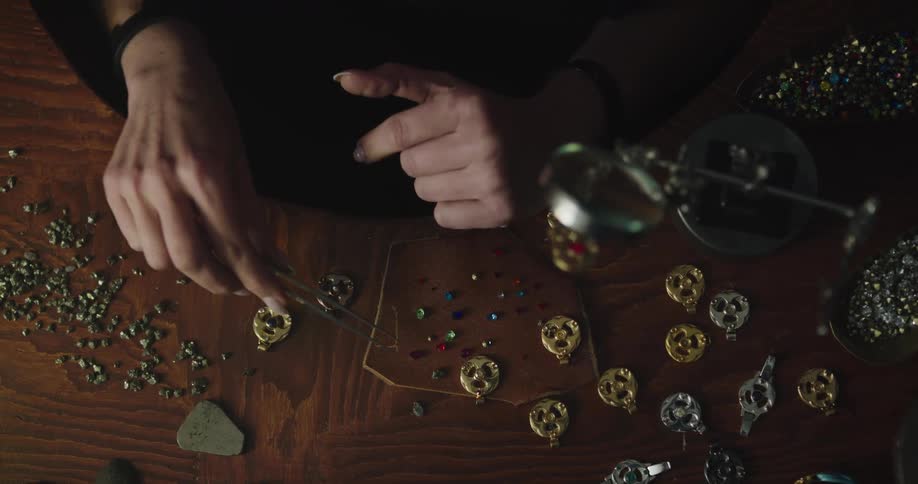 A jeweler picks up gem stones with tweezers for placement in gold and silver pendants