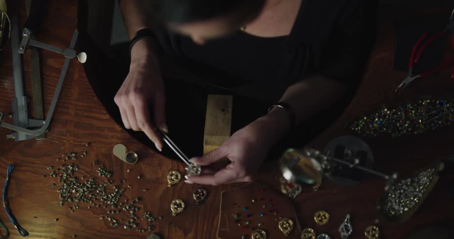 A jewelry designer applies beads to a piece using tweezers