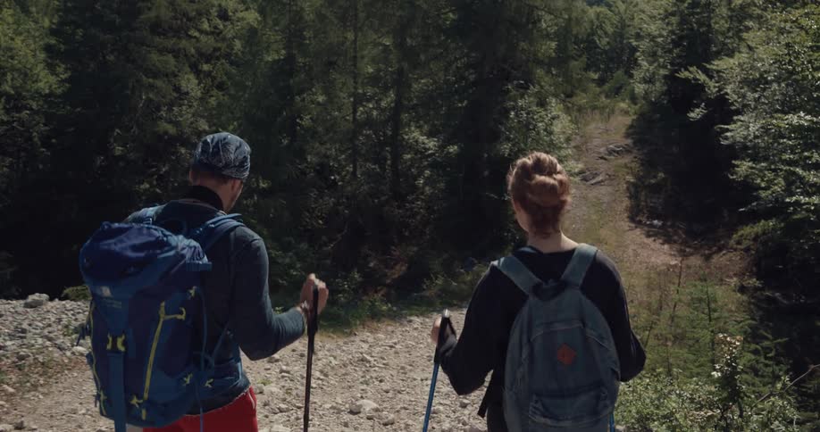 A man and woman hike down a rocky hill in a forest area