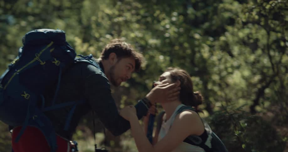 A man and woman hiking and hugging and kissing on the trail looking sad