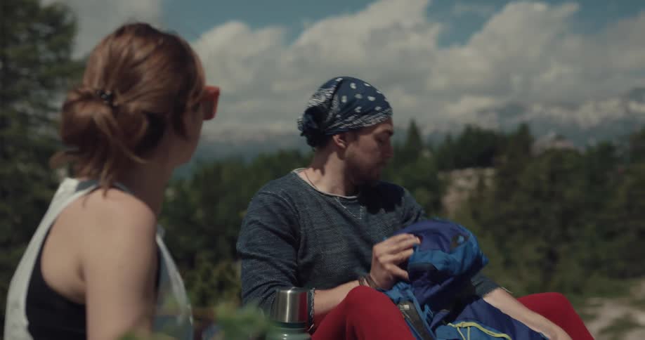 A man and woman unpack food and drinks while sitting on a mountain
