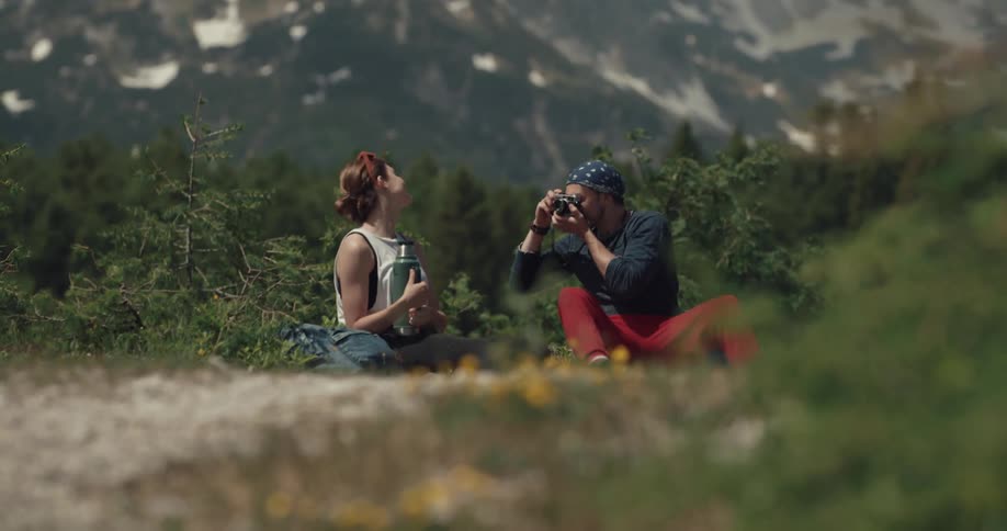 Woman hugs a thermos as her boyfriend takes her photo outdoors near the mountains