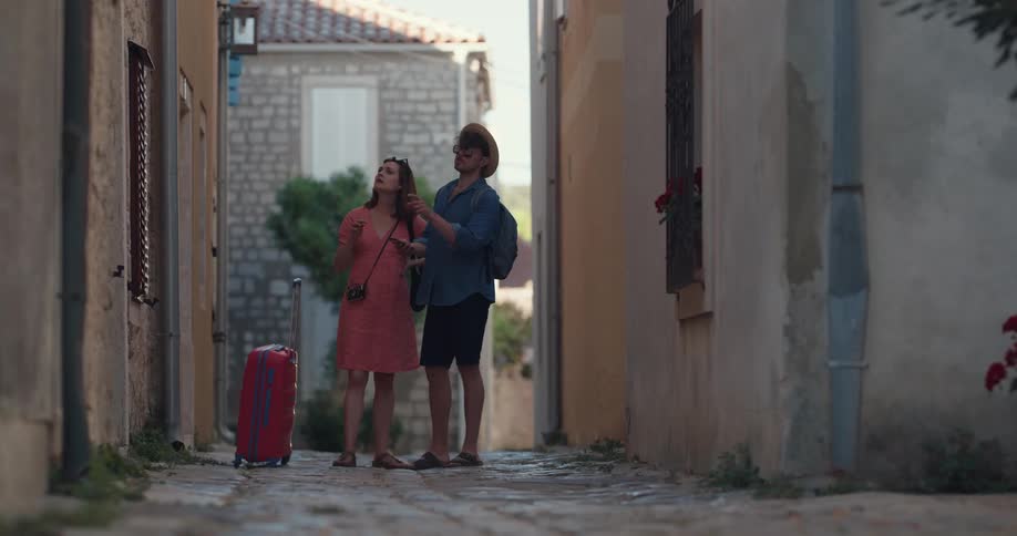 A man and woman traveling stand in between buildings and look at a cell phone as they look around