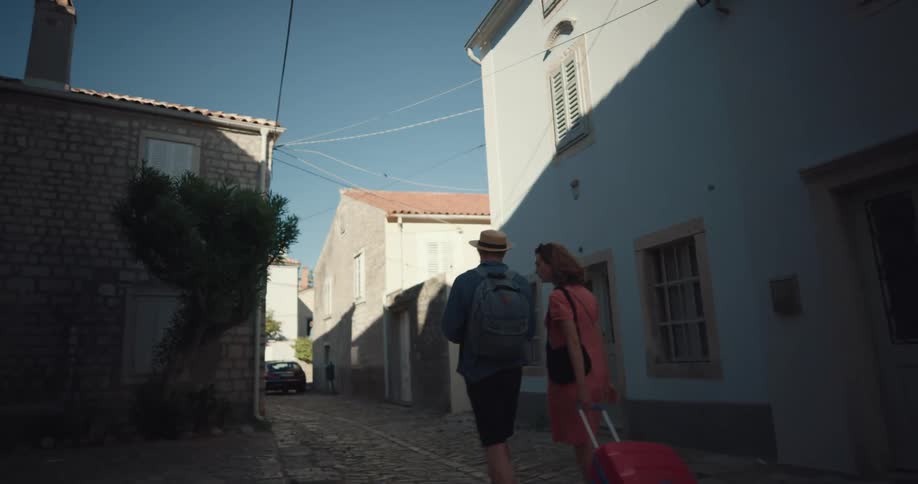 Woman pulls a suitcase while walking with a man in an alley in a foreign country