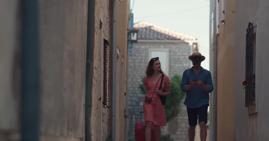 A man and woman walking around outdoors in an alley with suitcases
