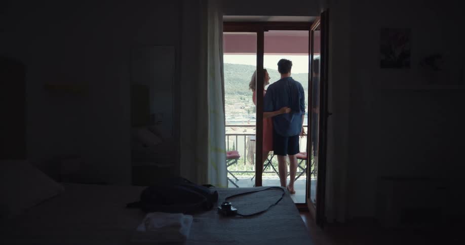 A man and a woman dance playfully and exit a room onto a balcony then proceed to embrace and kiss each other