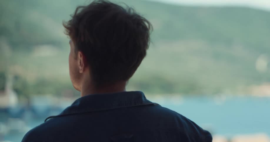 A man stands and looks out at a beach next to a mountainside during the day