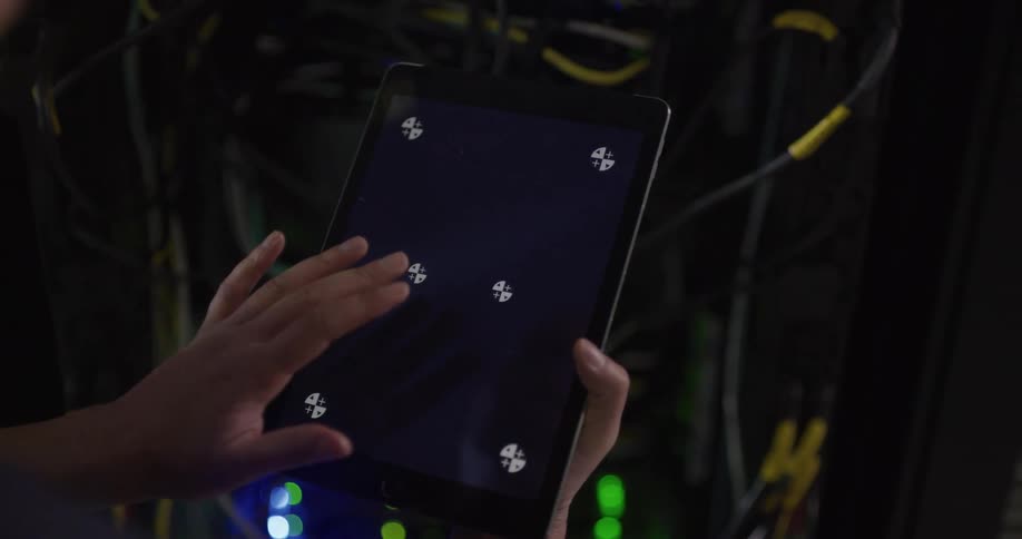 A person in a room using a tablet with a server and wires in the background