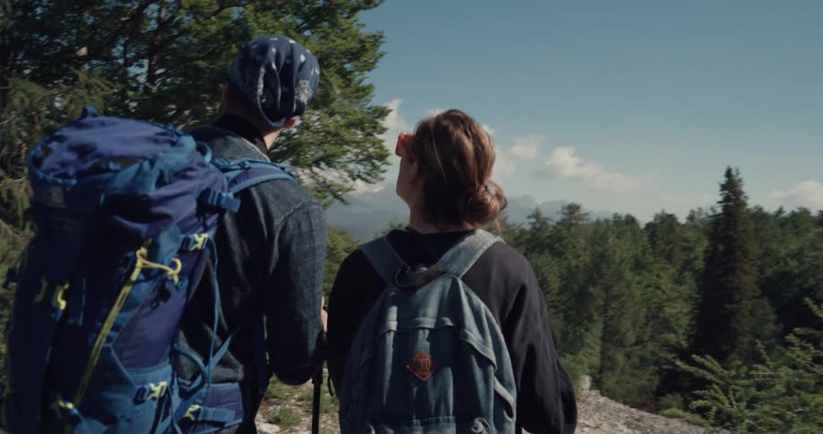 A man and woman in a forest hiking with trees the sky and clouds in the background