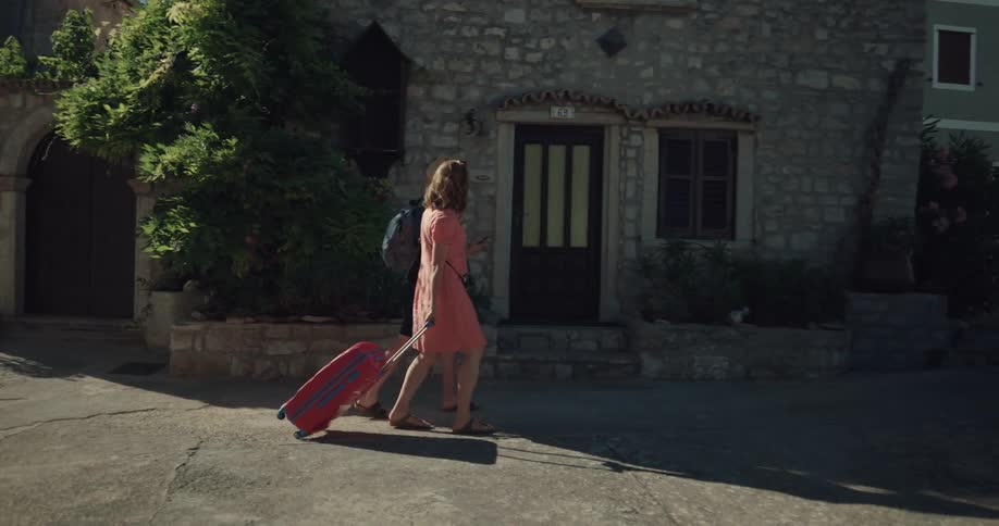 Man and woman walk down street with luggage using smartphone to navigate