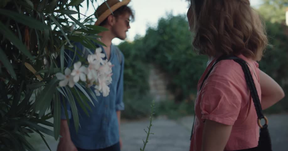 Traveling couple carrying luggage stops to smell the flowers in the countryside