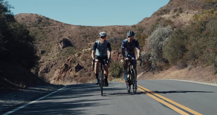 Friends cycle along road through low mountains smiling and joking with each other