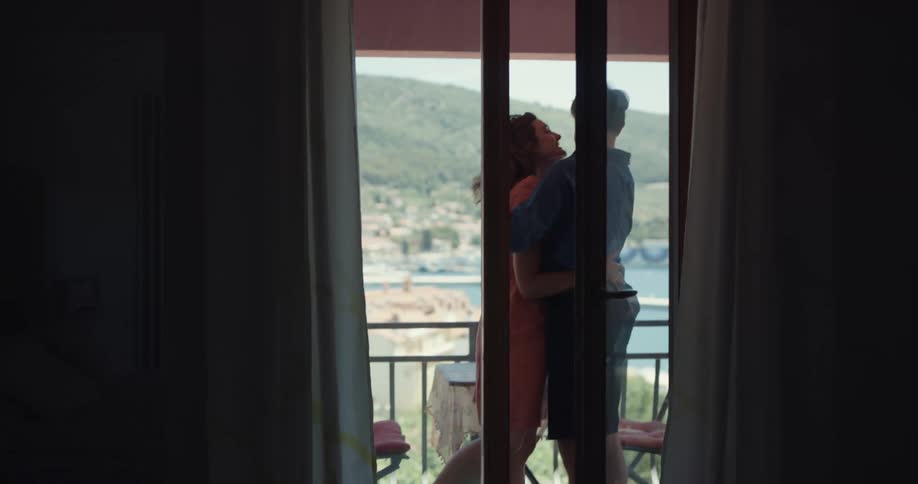 A couple walk into their hotel room drop their bags and head out to the balcony to celebrate with a hug and kiss