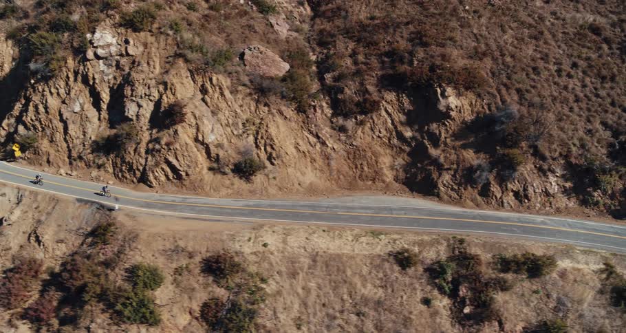A pair of cyclists ride bicycles along a winding road on a mountainside during the day