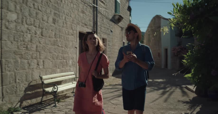 Couple walks along alley between buildings pulling luggage and using smartphone to navigate